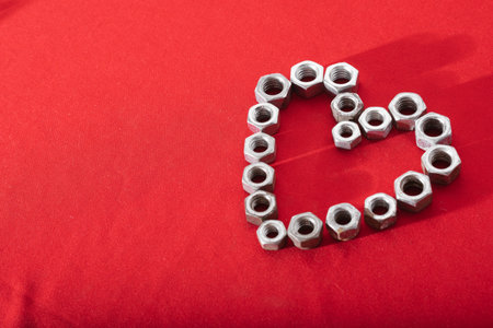 Heart made of steel nuts on red background, concept of love, peace and kindness, leaving space for advertising textの写真素材