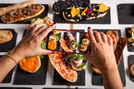 A female food blogger takes photos of the dishes on the restaurant table. Top view. Friends lunch, social media backgroundsの写真素材