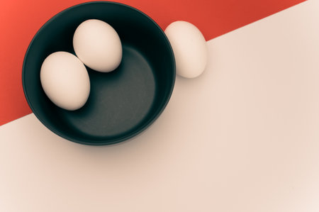 organic white eggs in a dark gray bowl on a white red surface with copy space for textの写真素材