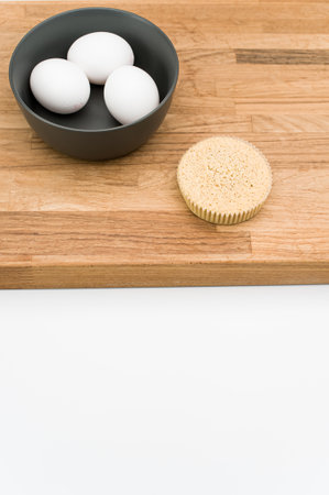 organic cake in a paper backing cup and bowl with eggs on a wooden chopping board on white...