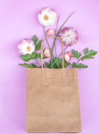 Paper bag with parsley, chives and garlic. Pink background.の写真素材