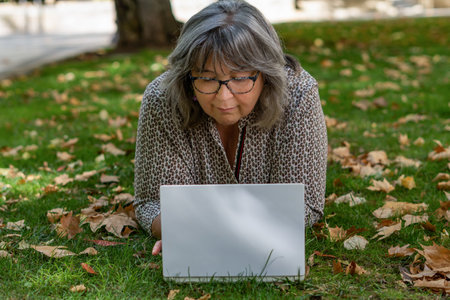 older white-haired woman with glasses with her computer in the park