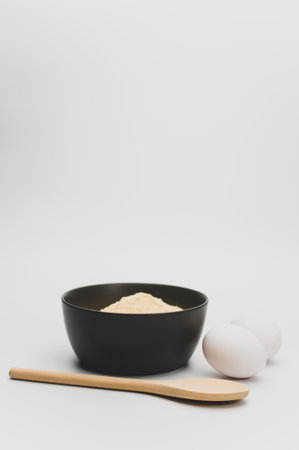 wooden spoon white eggs and dark gray bowl with wholegrain flour on white background with copy spaceの写真素材