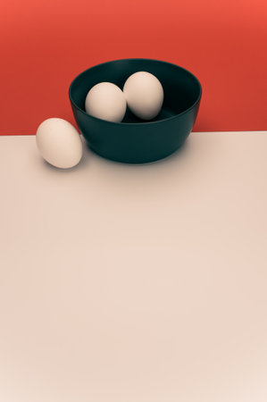 organic white eggs in a dark gray bowl on a white red surface with copy space for textの写真素材
