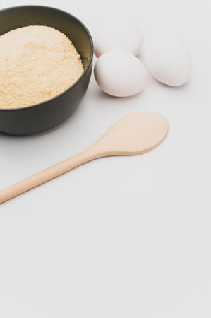 wooden spoon white eggs and dark gray bowl with wholegrain flour on white background with copy spaceの写真素材