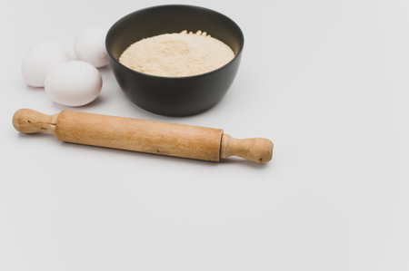 wooden rolling pin white eggs and dark gray bowl with wholegrain flour on white background with copy spaceの写真素材