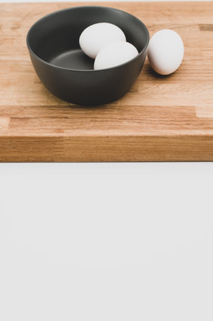organic white eggs in a dark gray bowl and wooden chopping board on a white surface with copy space...