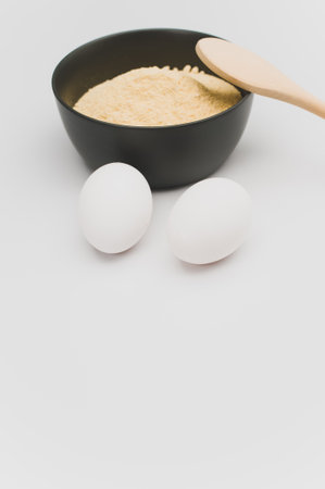 wooden spoon white eggs and dark gray bowl with wholegrain flour on white background with copy spaceの写真素材