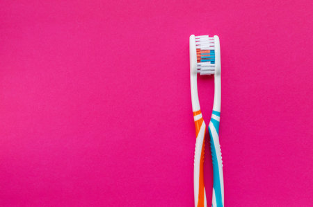 Two multi-colored toothbrushes on a pink background. The view from the top. Close up.The concept of...