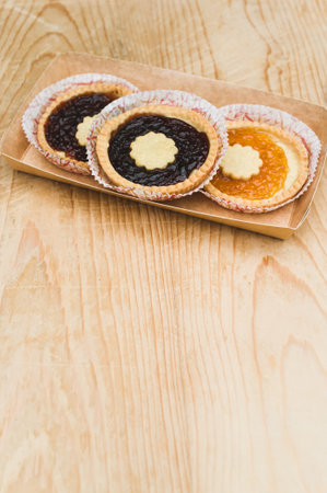 isolated apricot and cherry jam tart in a paper backing cup on a wood tabletop background with text spaceの写真素材
