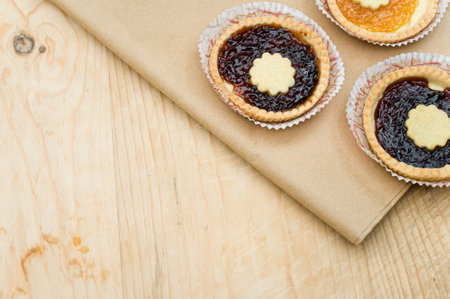 isolated apricot and cherry jam tart on a wood and brown paper tabletop background with text space