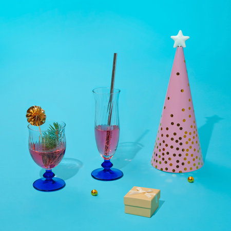 Business celebration with the pink cocktails and abstract conus christmas tree with star and confetti. The scene is decorated with indigo blue glasses, a small gift box, and miniature golden balls.の写真素材