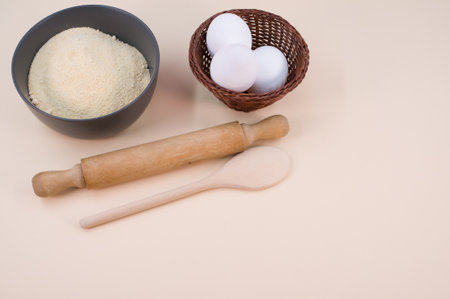 wooden rolling pin white eggs and dark gray bowl with wholegrain flour on beige background with copy...