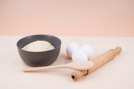 wooden rolling pin white eggs and dark gray bowl with wholegrain flour on beige background with copy spaceの写真素材