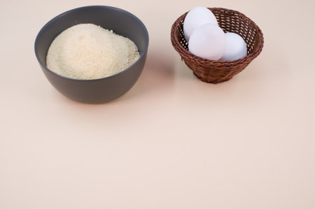 white eggs and dark gray bowl with wholegrain flour on beige background with copy space