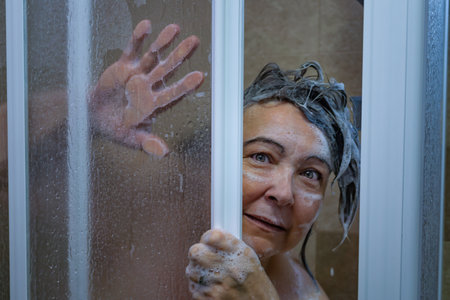 woman surprised while showering full of soap peeking out the doorの写真素材