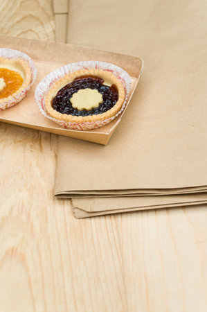isolated apricot and cherry jam tart in a paper backing cup on a wood tabletop background with text spaceの写真素材