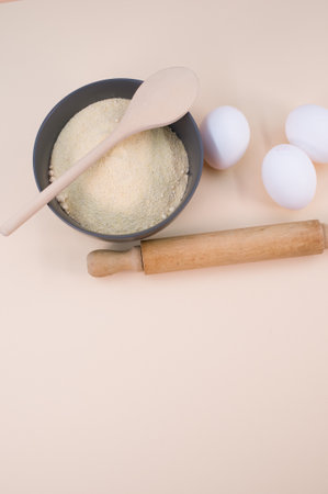 wooden rolling pin white eggs and dark gray bowl with wholegrain flour on beige background with copy spaceの写真素材