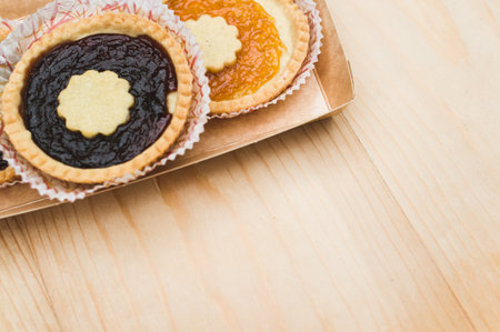 isolated apricot and cherry jam tart in a paper backing cup on a wood tabletop background with text spaceの写真素材