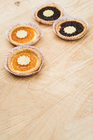 isolated apricot and cherry jam tart in a paper backing cup on a wood tabletop background with text spaceの写真素材