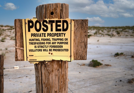 No Trespassing sign on old rustic fence post with desolate landscape and blue, cloudy skyの写真素材