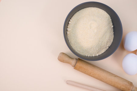 wooden rolling pin white eggs and dark gray bowl with wholegrain flour on beige background with copy spaceの写真素材