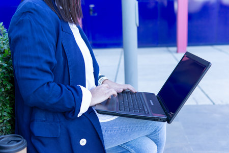 Unrecognizable beautiful Caucasian businesswoman using a laptop computer sitting outside an office building.の写真素材