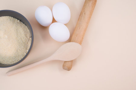 wooden rolling pin white eggs and dark gray bowl with wholegrain flour on beige background with copy spaceの写真素材
