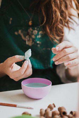 Artisan woman glazing a small ceramic pot. Preparation for making jewelry. Concept of hand crafting.