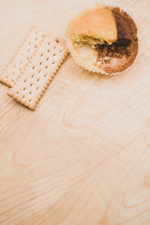 nibbled organic chocolate cupcake and biscuits on a rough wooden background with text spaceの写真素材