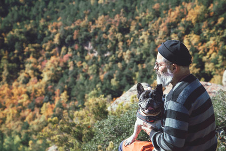 Man sitting with dog on rock looking at landscape on mountain cliffの写真素材