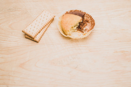 nibbled organic chocolate cupcake and biscuits on a rough wooden background with text space