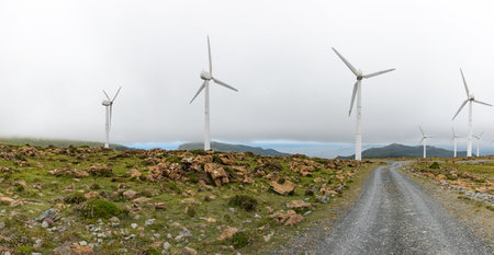 Beautiful windmills with sea background in Galicia, Spain with a road, produce electricity with wind turbinesの写真素材