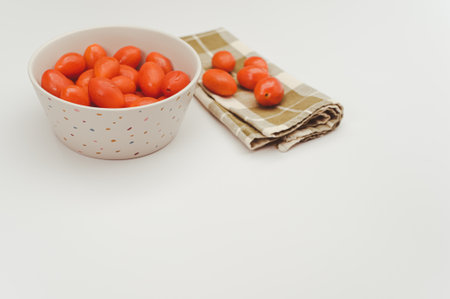 white decorated stoneware bowl full of datterini tomatoes on a white surface with text spaceの写真素材