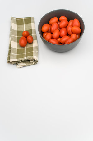dark gray stoneware bowl full of datterini tomatoes and table napkin on a white surface with text spaceの写真素材