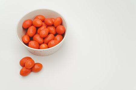 white decorated stoneware bowl full of datterini tomatoes on a white surface with text spaceの写真素材