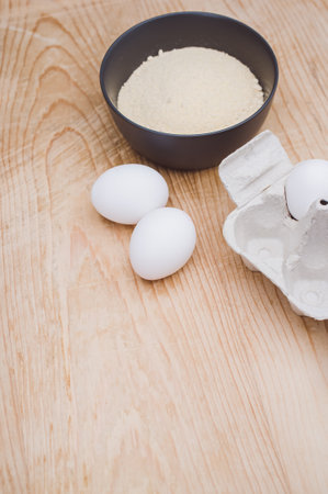 white eggs and dark gray bowl with wholegrain flour on worn wooden background with copy spaceの写真素材