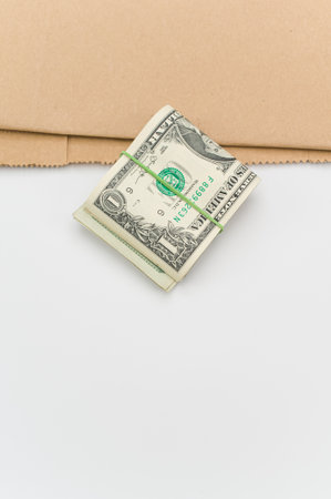 US dollar banknotes wad and brown paper on a white tabletop with text spaceの写真素材