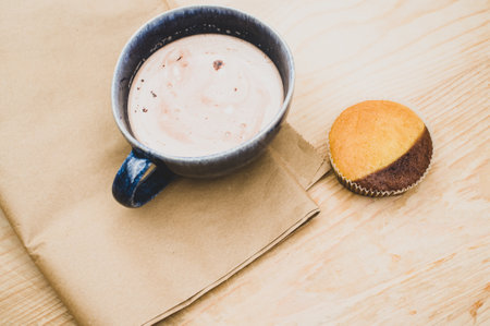 hot milk with cocoa in a blue cup and tasty cupcake on a rustic wooden and brown paper backgroundの写真素材
