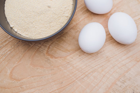 white eggs and dark gray bowl with wholegrain flour on worn wooden background with copy spaceの写真素材