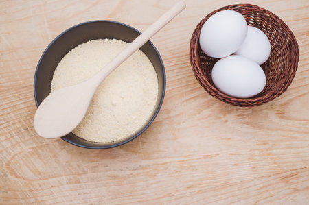 white eggs and dark gray bowl with wholegrain flour on worn wooden background with copy spaceの写真素材
