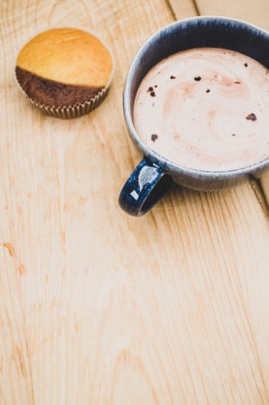 hot milk with cocoa in a blue cup and tasty cupcake on a rustic wooden and brown paper backgroundの写真素材