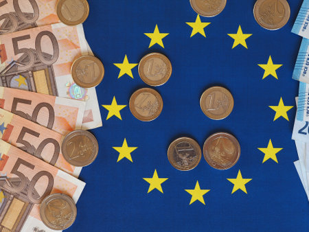 Euro banknotes and coins (EUR), currency of European Union over flag of Europeの写真素材