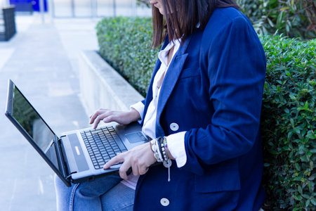 Unrecognizable beautiful Caucasian businesswoman using a laptop computer sitting outside an office building.の写真素材