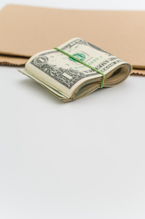 US dollar banknotes wad and brown paper on a white tabletop with text spaceの写真素材