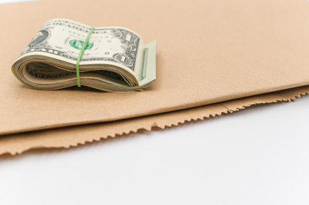 US dollar banknotes wad and brown paper on a white tabletop with text spaceの写真素材