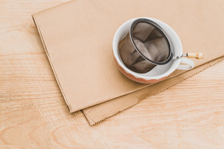 metal tea strainer and decorated tea cup on a kraft paper and wooden background with text spaceの写真素材