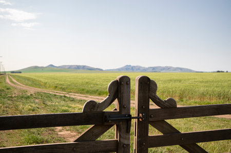 Rural landscape. Close-up of a gate overlooking the landscape of a green field with mountainsの写真素材