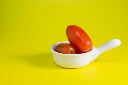 2 cherry tomatoes in white ceramic bowl on smooth yellow backgroundの写真素材
