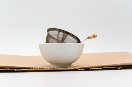 metal tea strainer with tea leaves in a ceramic bowl on a white background with text spaceの写真素材